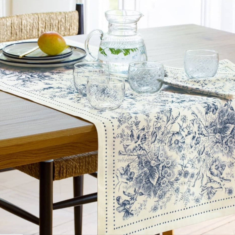 Dining table with floral-patterned table runner, glasses, and a pitcher.
