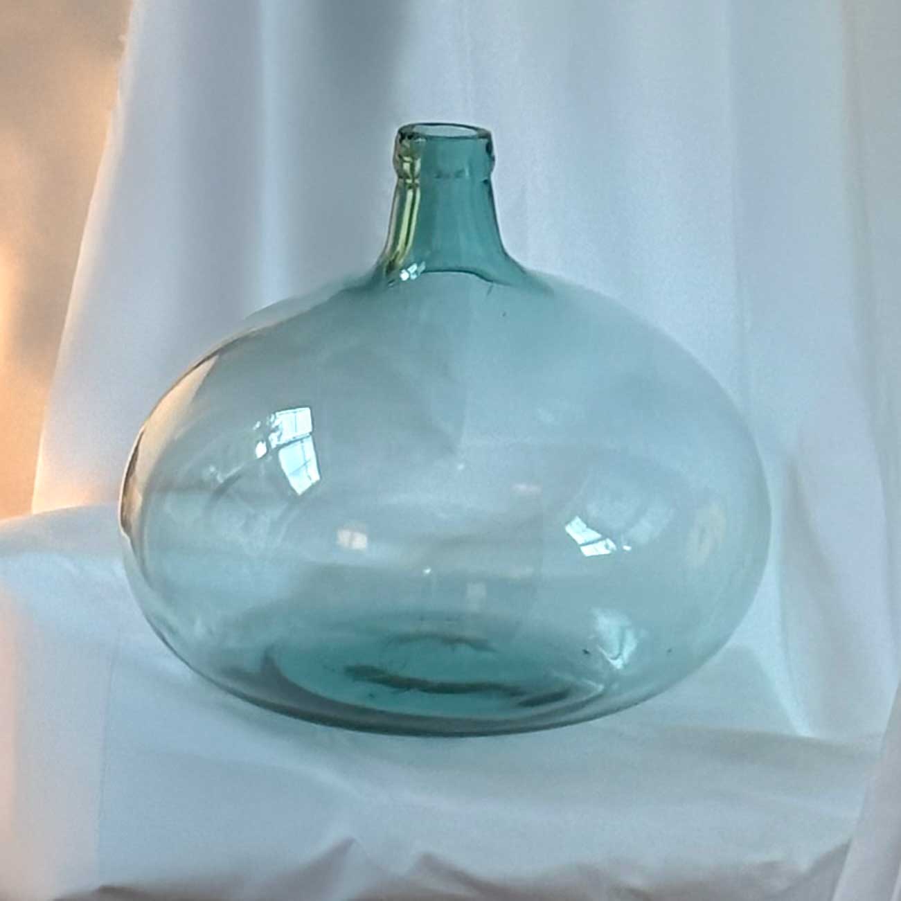 Large turquoise glass vase on a white surface with a neutral background