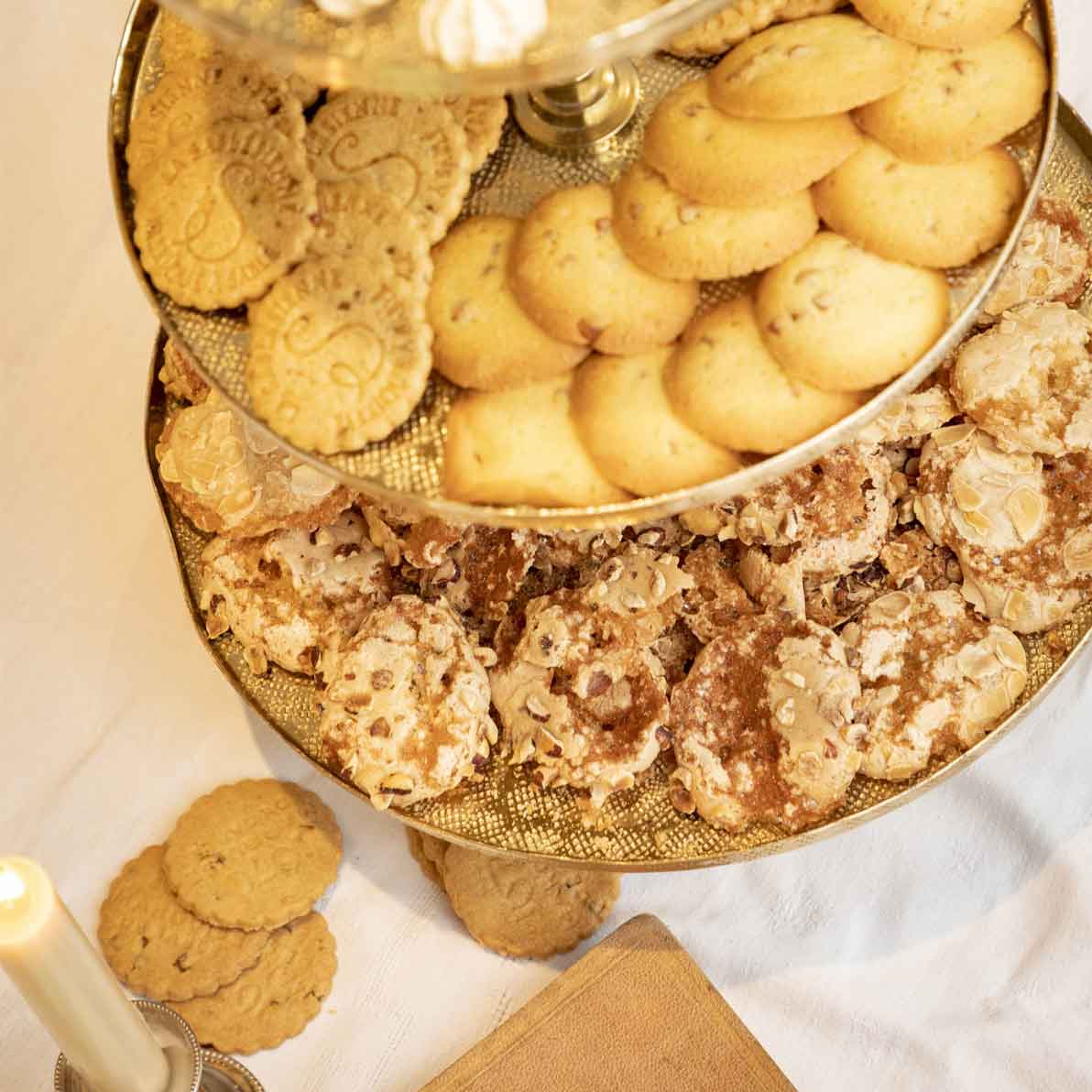 Assorted cookies on a gold platter with a candle and book in the background