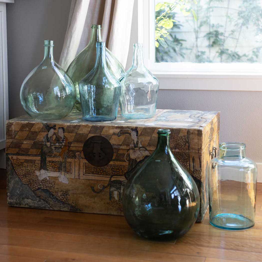 Collection of glass bottles on a wooden chest with a window in the background