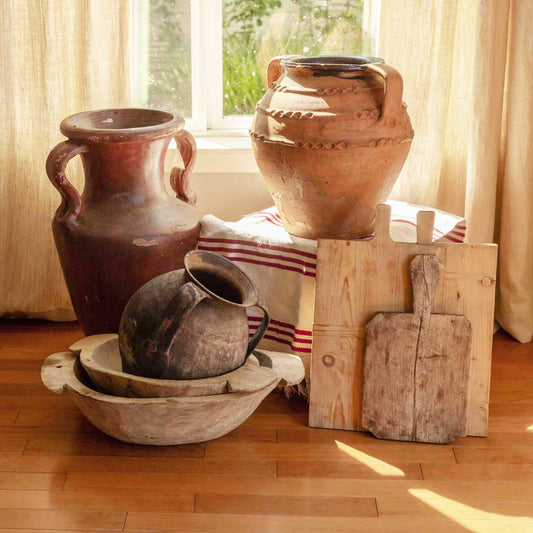 Vintage ceramic pots and wooden tools on a wooden floor with a window in the background