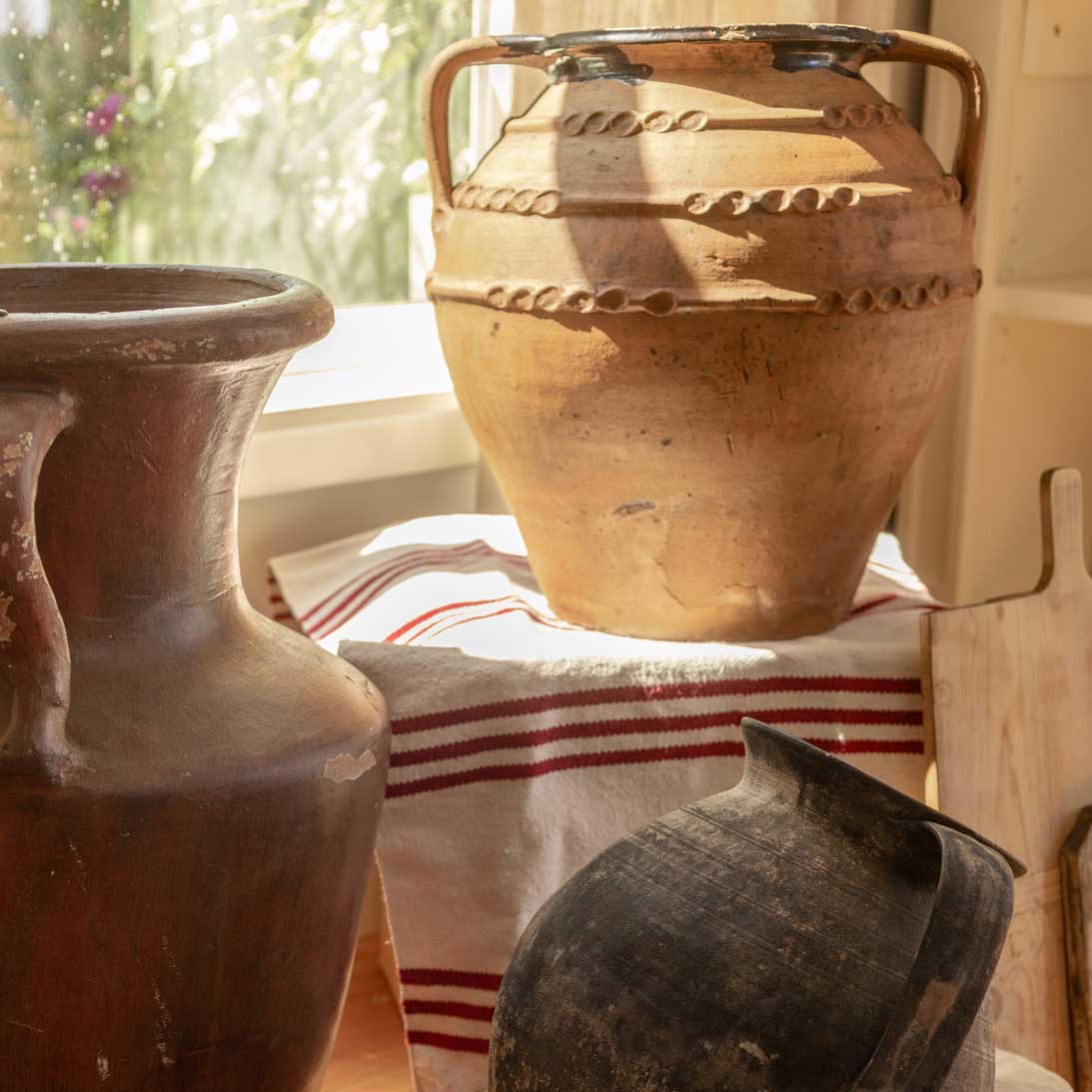 Three ceramic pots on a table with a striped cloth underneath, in a softly lit room.