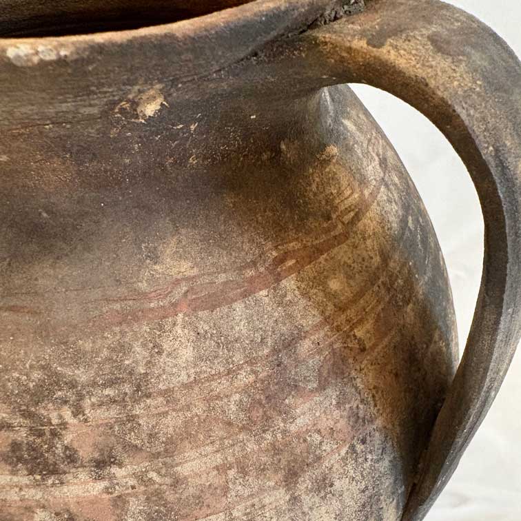 Close-up of a rustic, worn ceramic pitcher with a handle.
