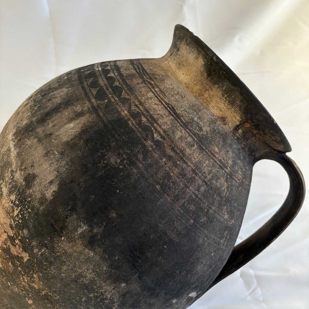 Ancient ceramic pitcher with decorative patterns on a white background