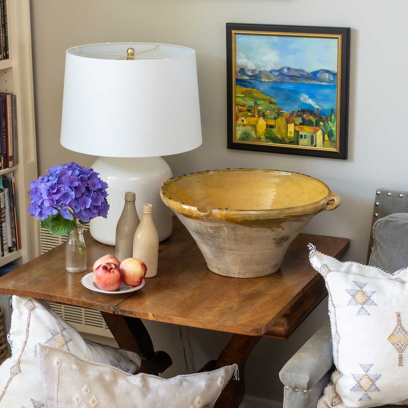 Decorative table with lamp, bowl, flowers, and fruit in a home setting.