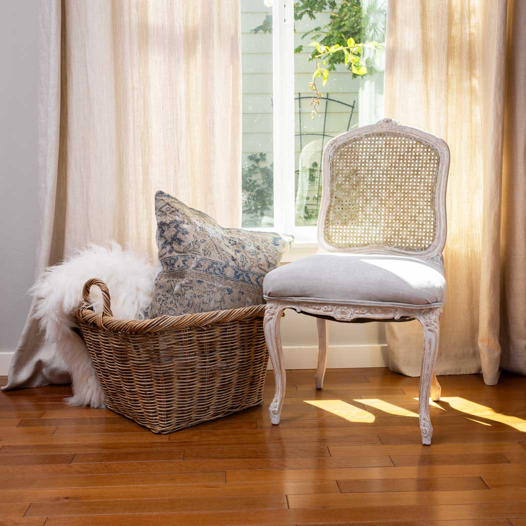 Chair with a woven backrest and cushioned seat next to a wicker basket with decorative pillows on a wooden floor.