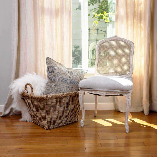 Chair with white cushion and wicker basket against a window with sheer curtains