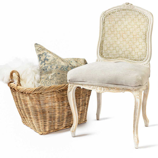 Decorative chair with wicker back and seat, next to a woven basket with a pillow on a white background