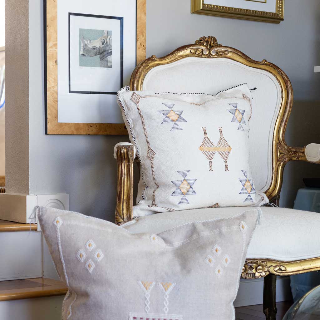 Decorative pillows with geometric patterns on a white armchair with gold accents.