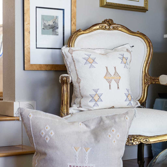 Decorative pillows with geometric patterns on a white armchair with gold accents.
